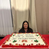 Susanna Scatizzi accanto a una grande torta natalizia con auguri dedicati alla famiglia dell’idrochinesiterapia.